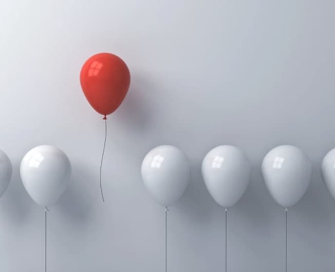 A red balloon rising above white balloons
