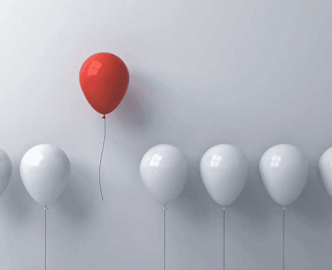 A red balloon rising above white balloons
